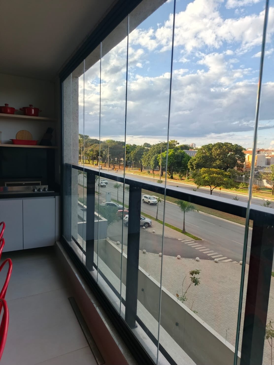 Varanda com cortina de vidro Balcony fechada, bancada gourmet e vista para avenida arborizada em Brasília