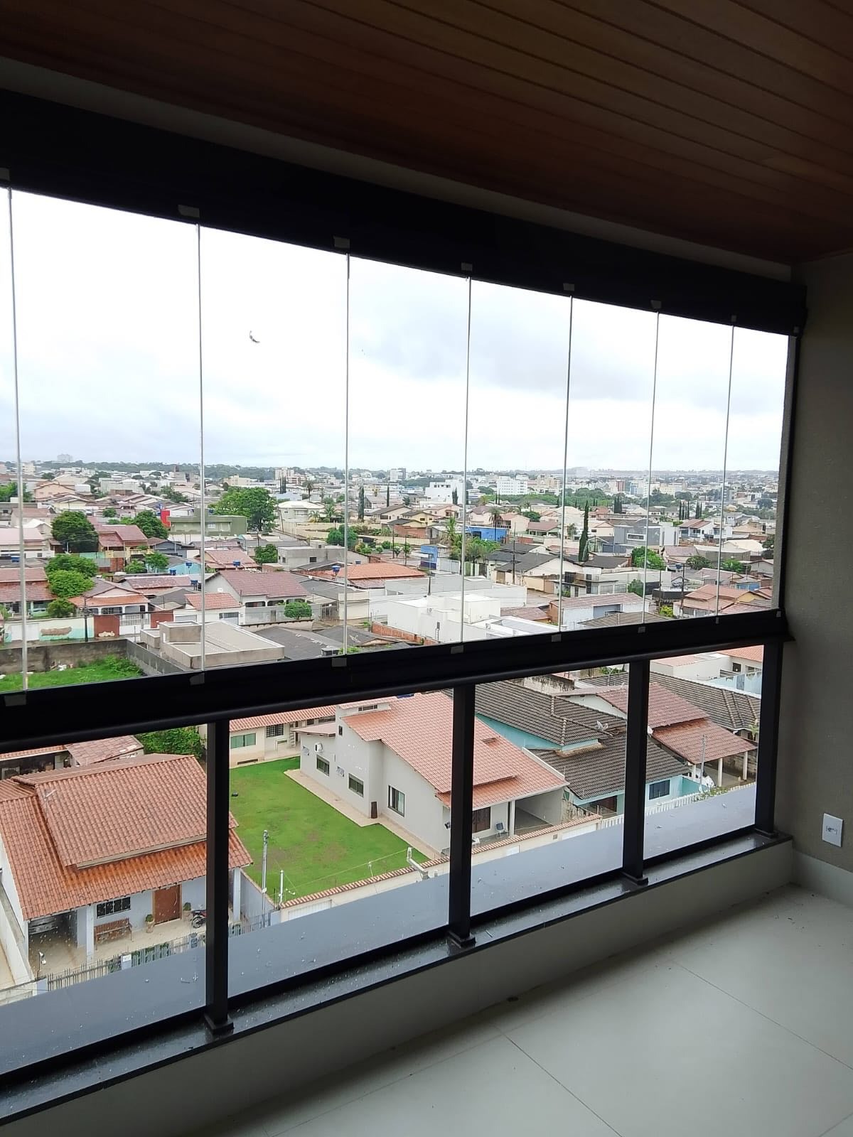 Varanda com cortina de vidro fechada e vista para bairro residencial